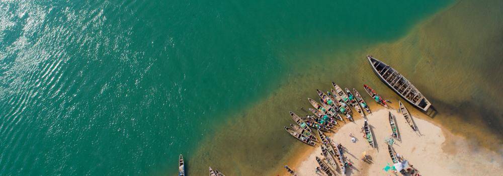 Aerial view of fishing boats parked on sand along a clear blue lake